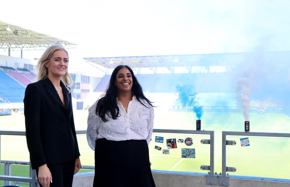 Justisminister Emilie Enger Mehl og kulturminister Lubna Jaffery smiler ved siden av to røykbomber på Intility Arena.